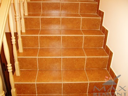 Schody wyłożone brązowymi, kwadratowymi płytkami ceramicznymi z jasną fugą, widok z góry, drewniana balustrada po lewej stronie.